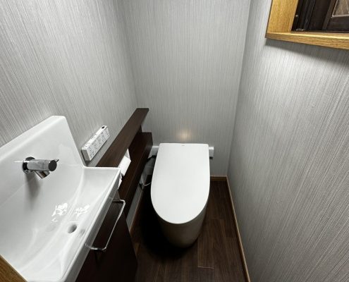 壁クロス・床材も張り替え、落ち着いた空間に生まれ変わったトイレ全景｜ストライプ柄のクロスと木目調クッションフロアで高級感ある仕上がり