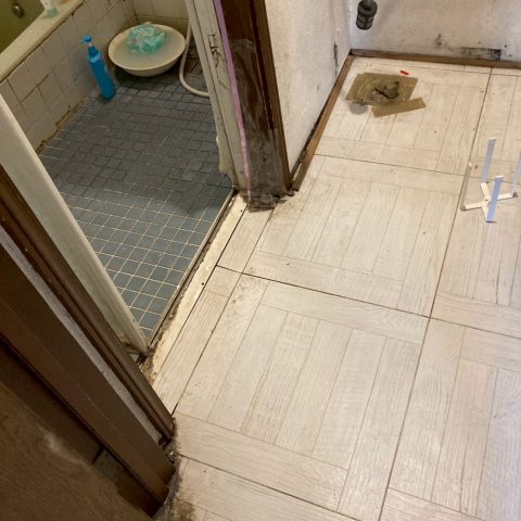 洗面脱衣所の施工前写真。床材の黒ずみやカビ、古くなったクロスが目立ち、リフォーム前の劣化状態が分かる。