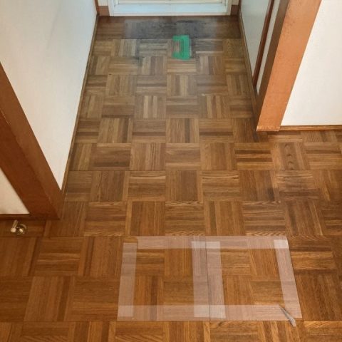 「玄関から廊下へ続く既存フローリングの沈み部分をテープでマーキングした施工前の様子