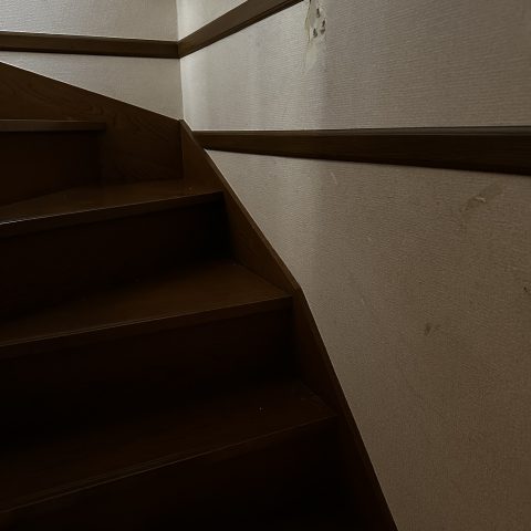 クロス張り替え前の階段壁｜手すりまわりに剥がれや黒ずみが見られる状態