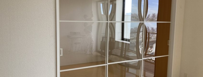リビングと洋室の間に設置されたガラス引戸。プレイススウィング3枚引戸仕様で、白フレームと段格子デザインが採光とプライバシーを両立した仕切り