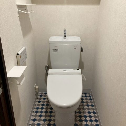 吊戸棚とベージュクロスでやや圧迫感のあるトイレ空間｜東京都大田区のトイレリフォーム施工前の様子」