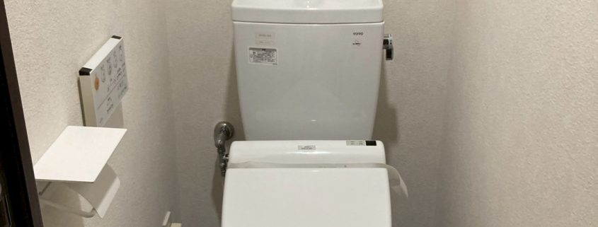 吊戸棚とベージュクロスでやや圧迫感のあるトイレ空間｜東京都大田区のトイレリフォーム施工前の様子」