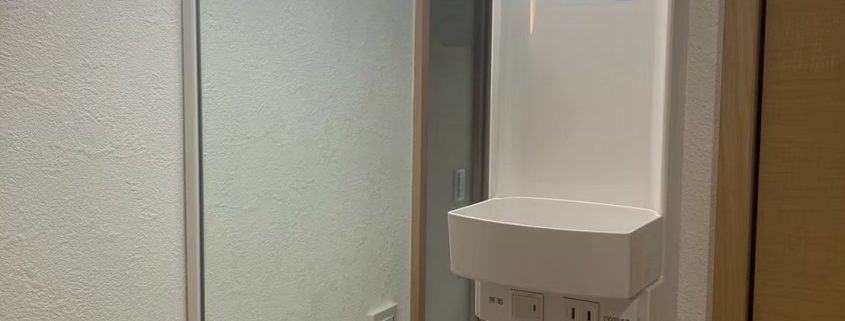 東京都大田区の賃貸マンション原状回復工事で交換した新しい洗面化粧台。LED照明付きミラーと白いクロスで明るく清潔感のある仕上がり