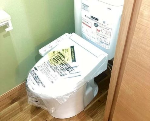 東京都大田区の賃貸マンションで原状回復工事により交換された最新型ウォシュレット付きトイレ。木目調の床とホワイト×グリーンのクロスで清潔感と快適性が向上した施工後の様子