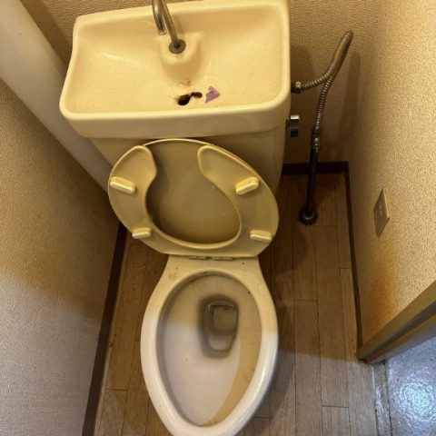 東京都大田区の賃貸マンション原状回復工事前のトイレ。老朽化したタンク一体型の便器と汚れが目立つ床材が使用されており、全体的に暗く古びた印象の施工前写真