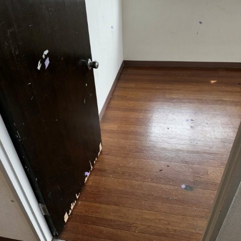 東京都大田区の賃貸マンションで、塗装剥がれや傷が目立つ古い室内ドアの交換前の様子。暗い色味で室内が重たく見える状態。