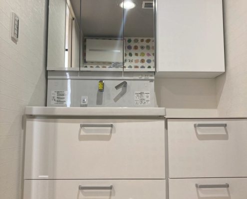 リフォーム前の洗面化粧台。横幅のある一体型カウンターと三面鏡の既存状態