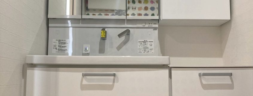 リフォーム前の洗面化粧台。横幅のある一体型カウンターと三面鏡の既存状態